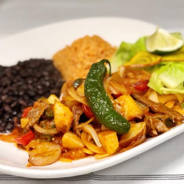 Mexican dish with stewed meat and vegetables, black beans, rice, and a lime wedge.