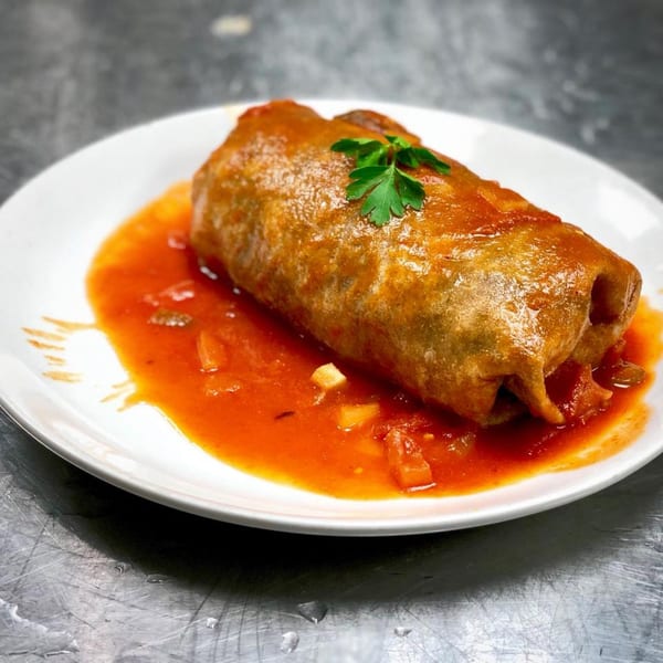 A large, golden-brown burrito covered in red sauce and garnished with parsley on a white plate.
