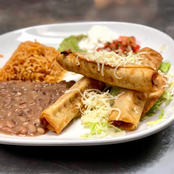 Mexican taquitos with rice, beans, guacamole, sour cream, and pico de gallo on a white plate.