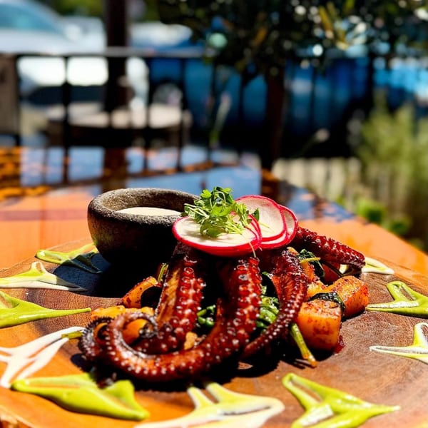 Grilled octopus with potatoes, radishes, and a side of sauce on a wooden board at Agave.