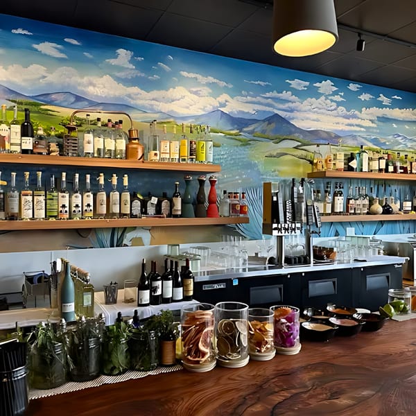 Agave restaurant's bar with a mountain mural, liquor bottles, and cocktail garnishes on a wooden counter.
