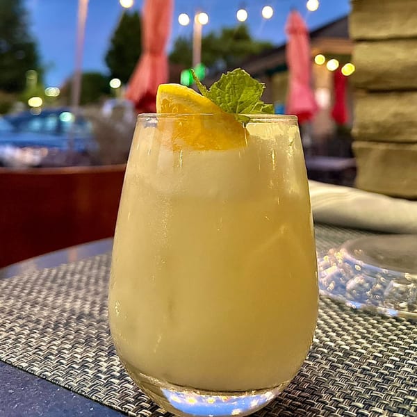 A refreshing Agave Mexican Restaurant cocktail with lemon and mint on an outdoor patio at dusk.