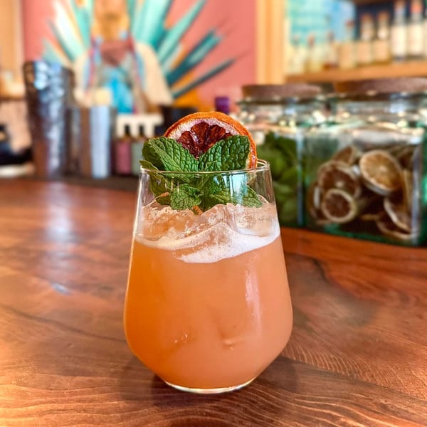 Agave's orange cocktail with mint and dried orange slice on a wooden bar.