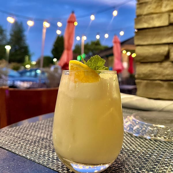 A refreshing Agave cocktail with a lemon slice and mint, on an outdoor patio at dusk.