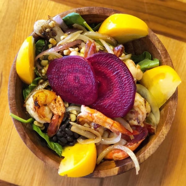 A vibrant Agave Mexican shrimp salad with beets, yellow tomatoes, and black beans in a wooden bowl.