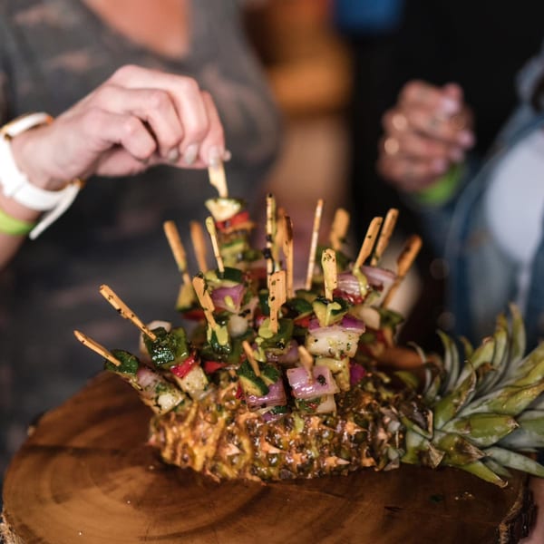 Mexican skewers with vegetables and shrimp, served in a pineapple on a wooden board.